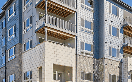 A building with balconies and a tree in front.
