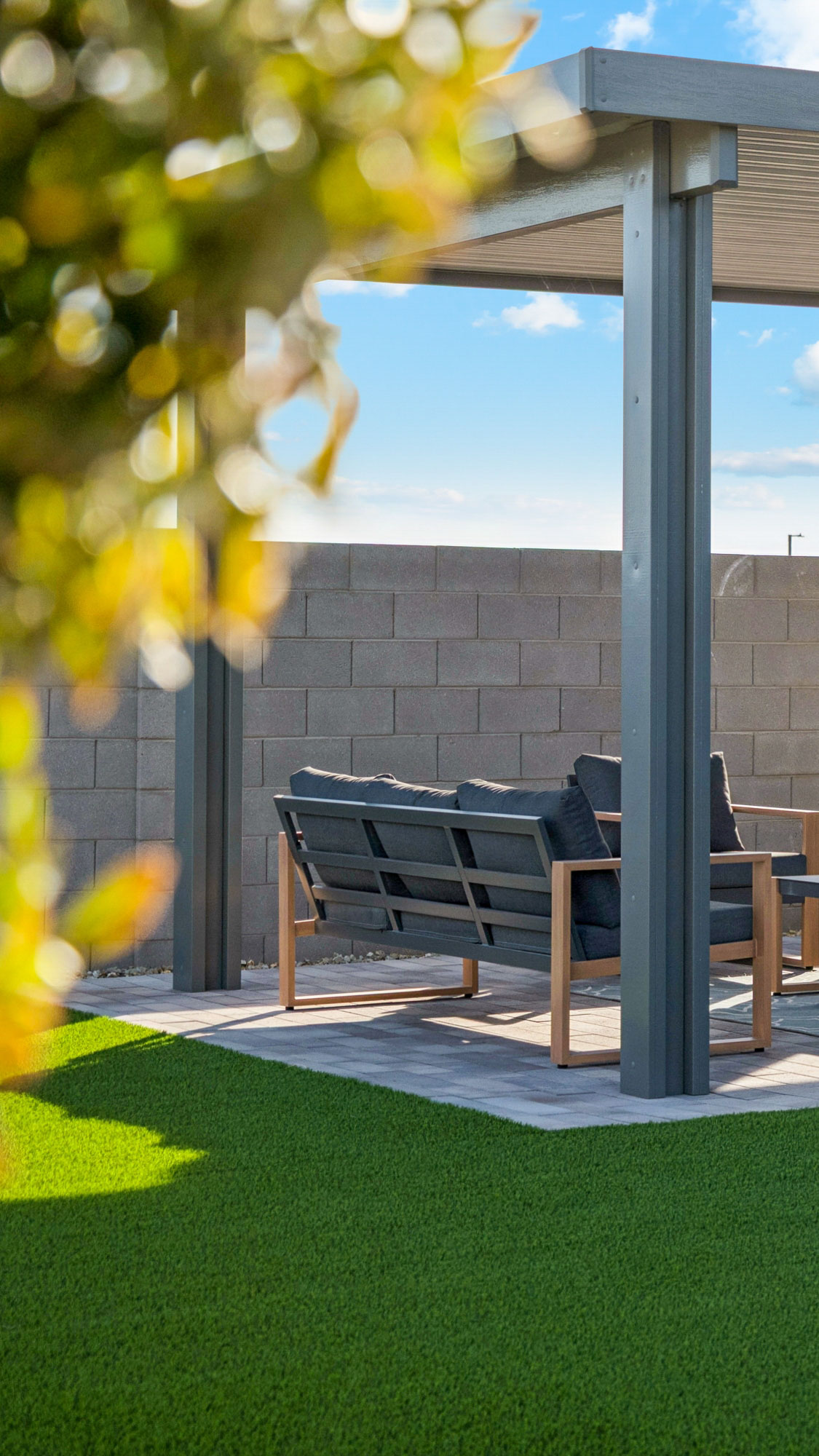 Backyard editorial photo with extended covered patio, anf furniture and turf grass surrounded by foliage- new construction homes near amarillo ranch palomino ranch in maricopa AZ with USDA new construction 