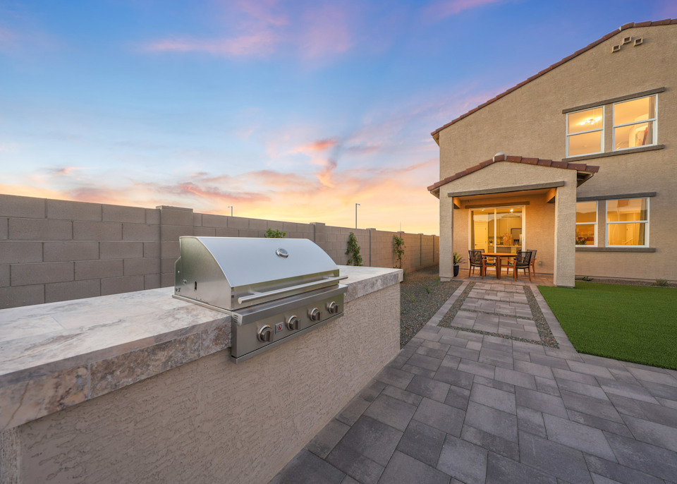 A brick patio with a brick wall and a brick walkway with a house and a blue sky.