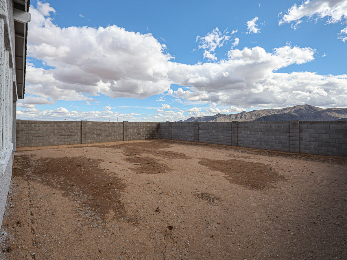 A dirt field with a fence and mountains in the background.