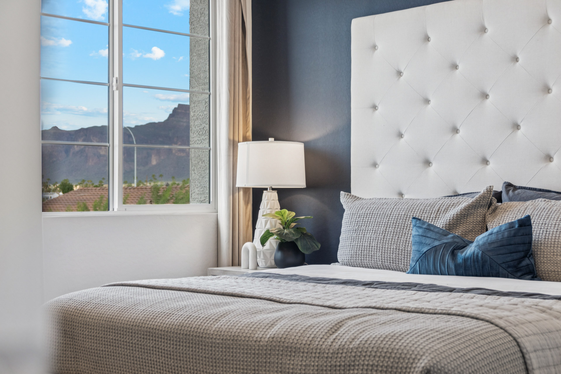 A bed with a lamp and a window with a view of a city.