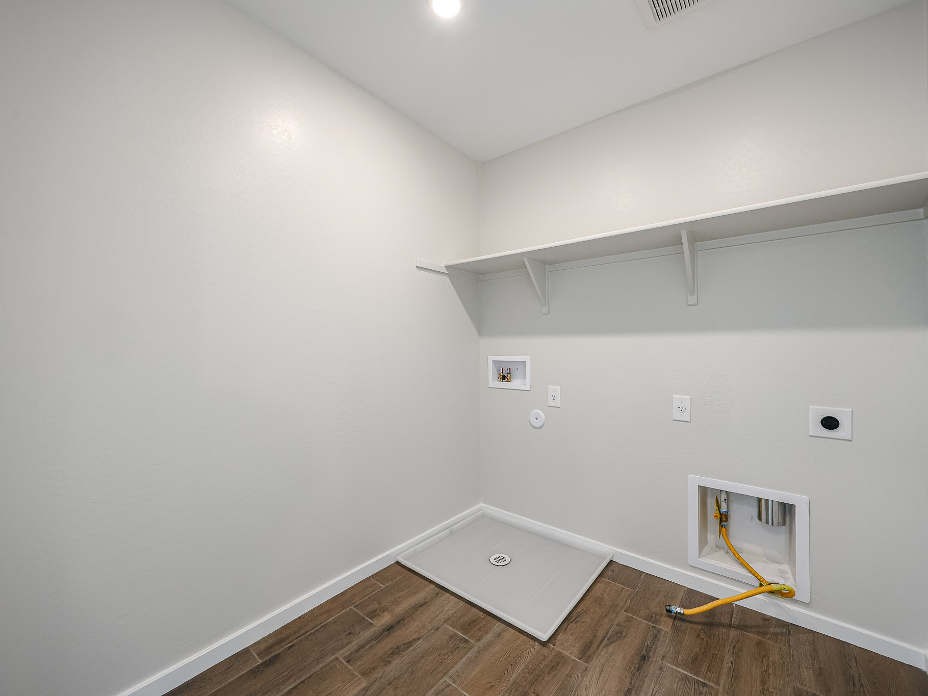 A room with a wood floor and a white wall with a yellow tape.