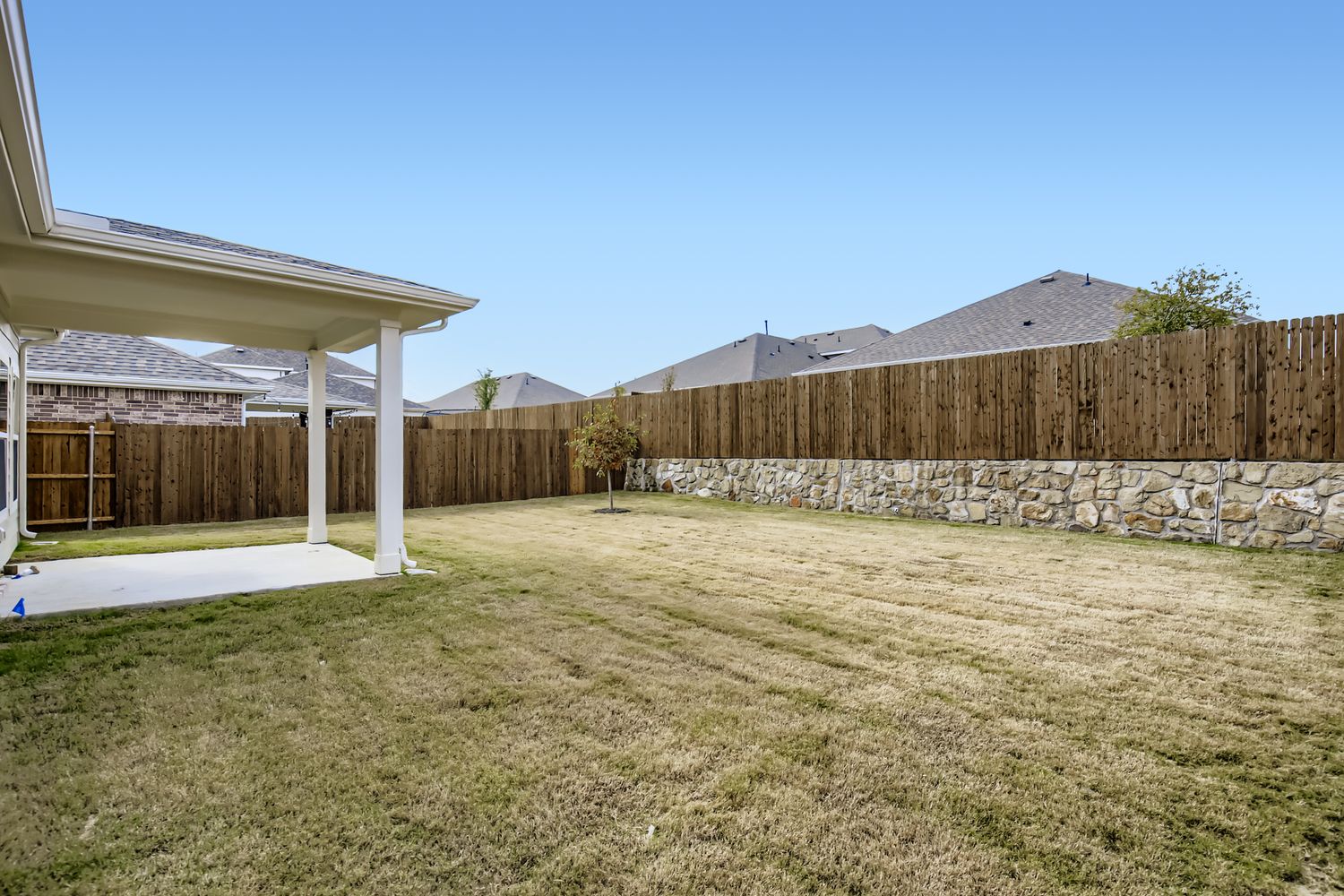 A fenced in yard with a stone wall and a tree.