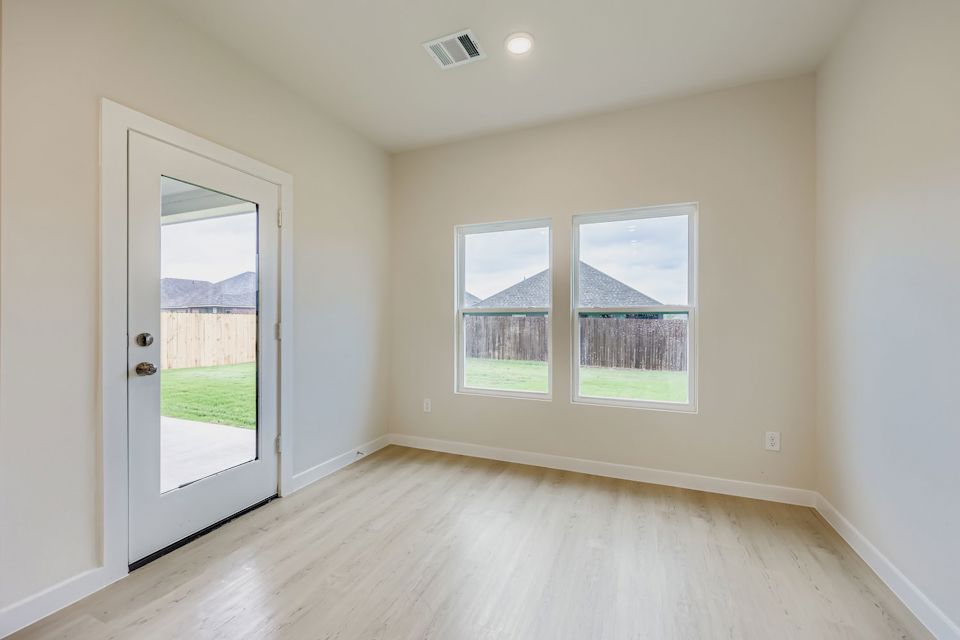 A room with a wood floor and a window with a view of a field and a house.