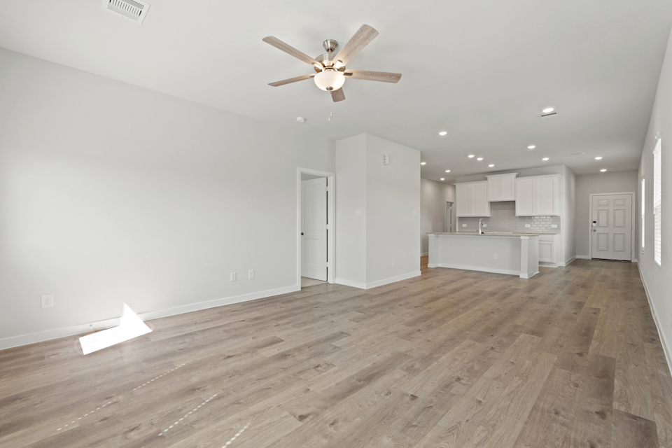 A large empty room with a ceiling fan and white cabinets.