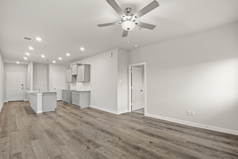A large empty room with a ceiling fan and white cabinets.