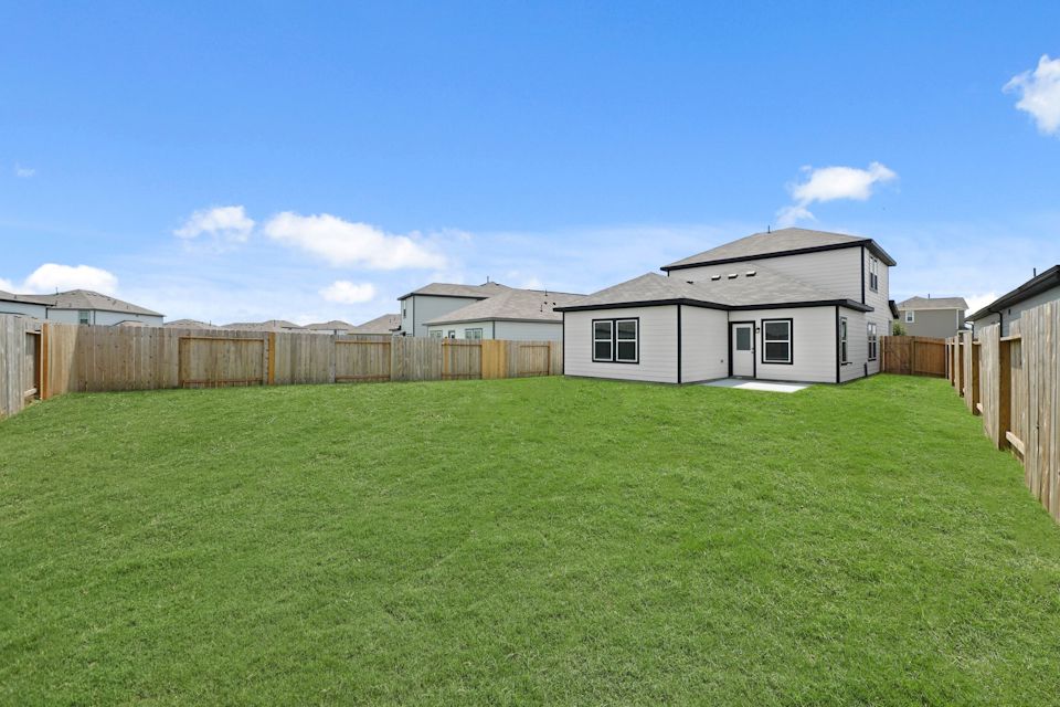 A grassy yard with a fence and a house in the background.