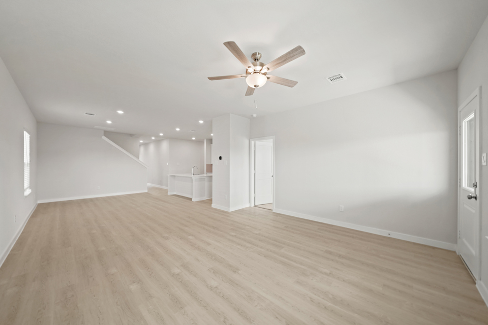 A large empty room with a ceiling fan and a wood floor.