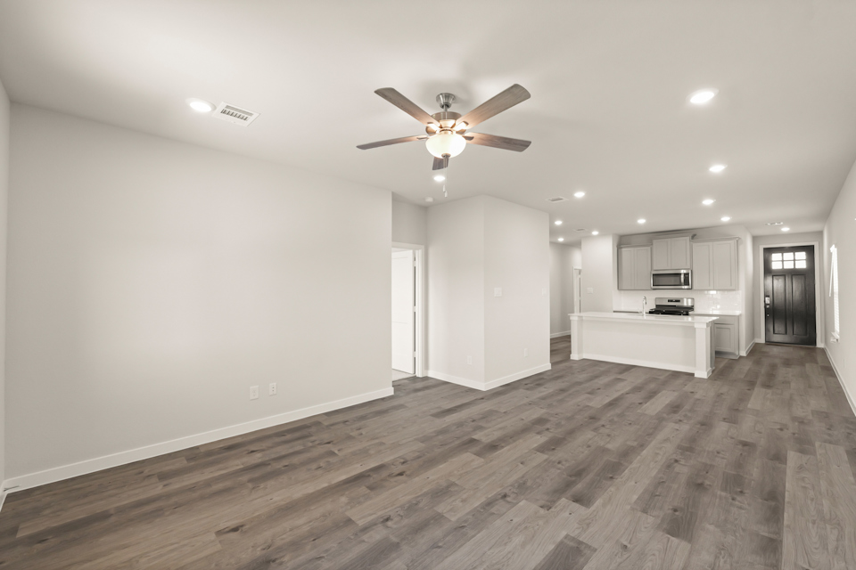 A large empty room with a ceiling fan and a wood floor.