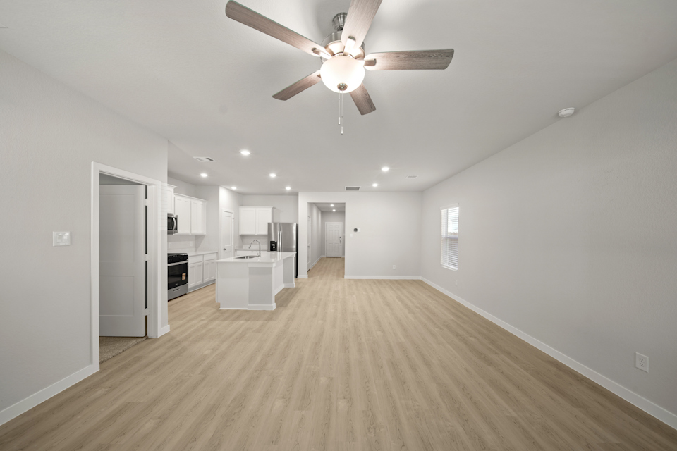 A large empty room with a ceiling fan and a wood floor.