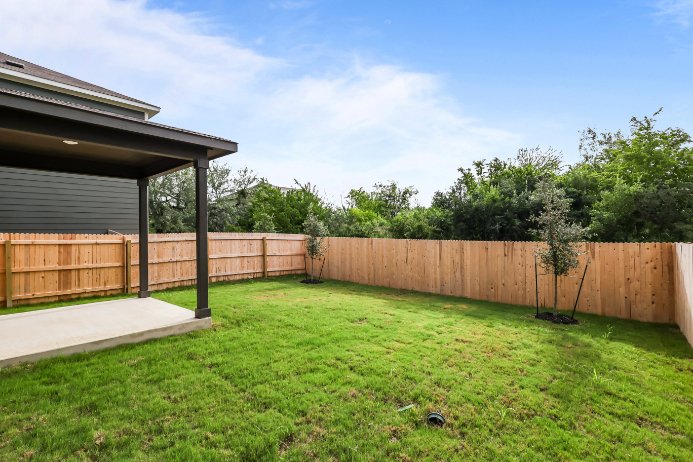 A backyard with a fence and a tree with Darwin D. Martin House in the background.