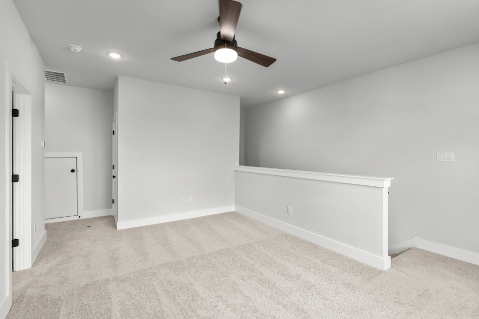 A room with a ceiling fan and a white wall.