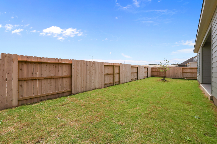 A fenced in yard with a tree and a building in the background.