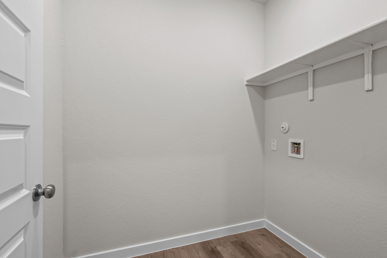 A white wall with a white door and a wood floor.