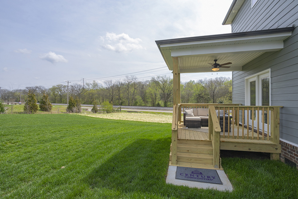 A deck with a railing and a house with a yard and trees in the background.